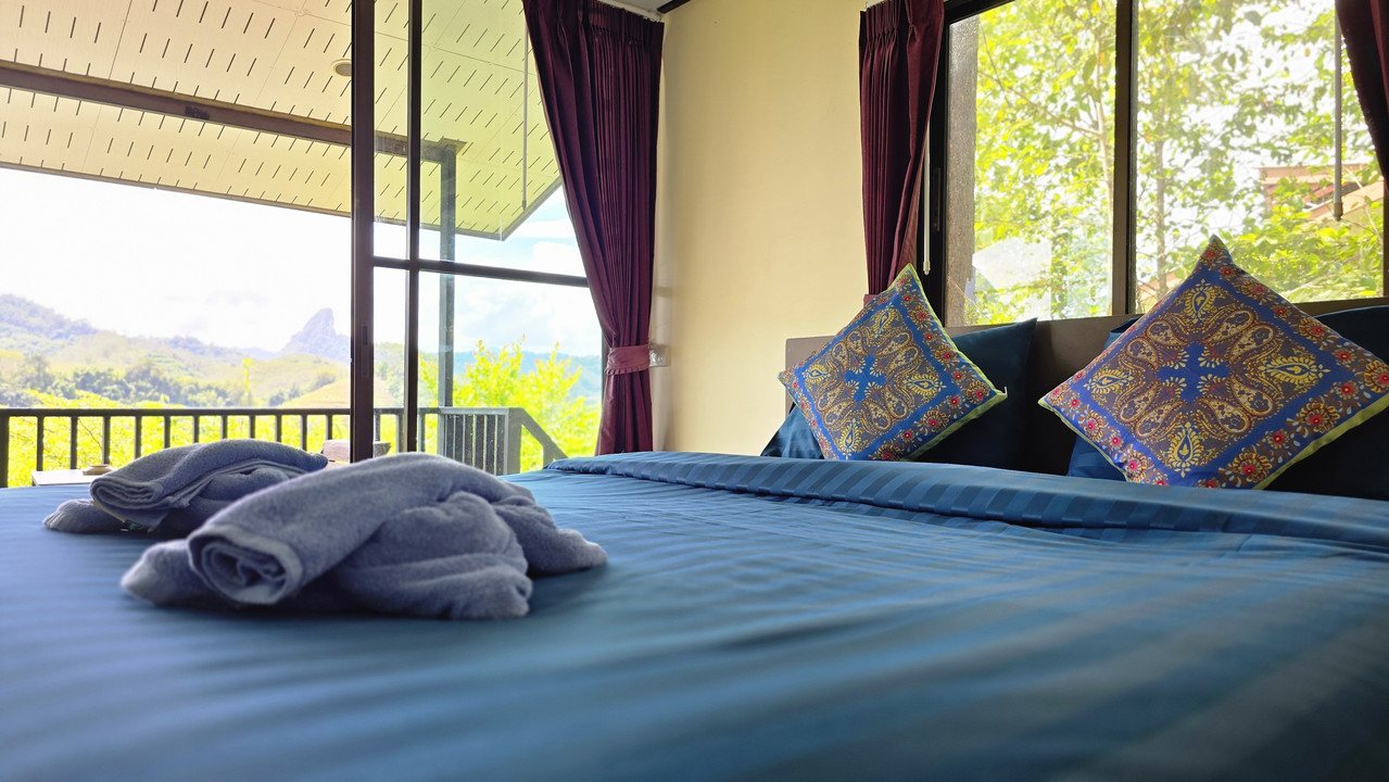 Bed facing floor-to-ceiling windows over the Khao Sok mountains